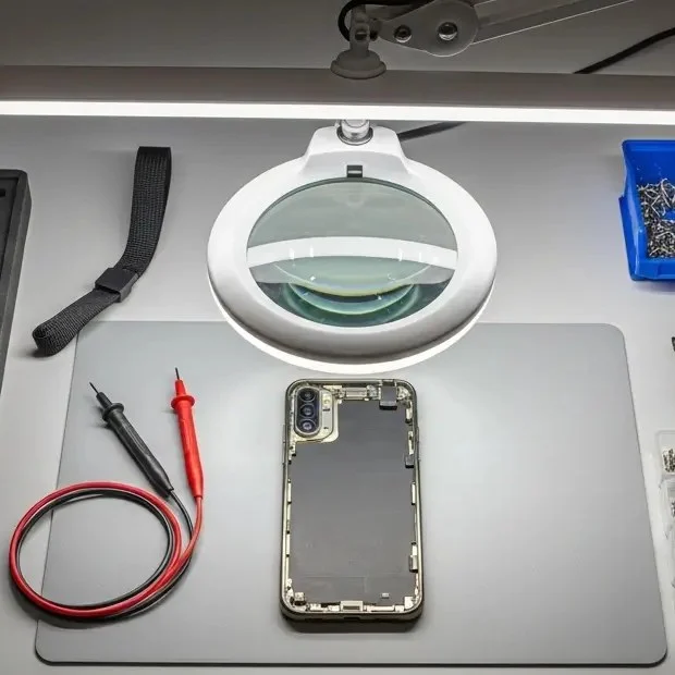 Lente d'ingrandimento, smartphone aperto e puntali del tester su un tappetino da lavoro